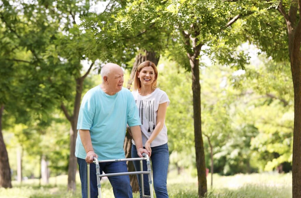 a woman helps a senior man with a walker walk through the park