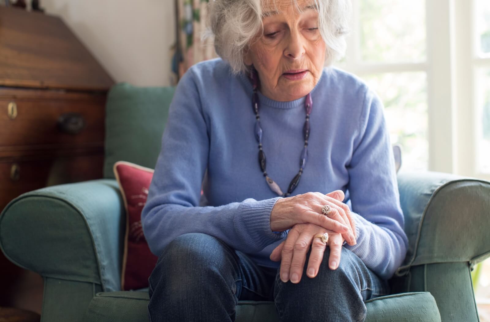 A senior woman sits on the couch, her posture conveying a gesture of loneliness as she reflects in solitude.