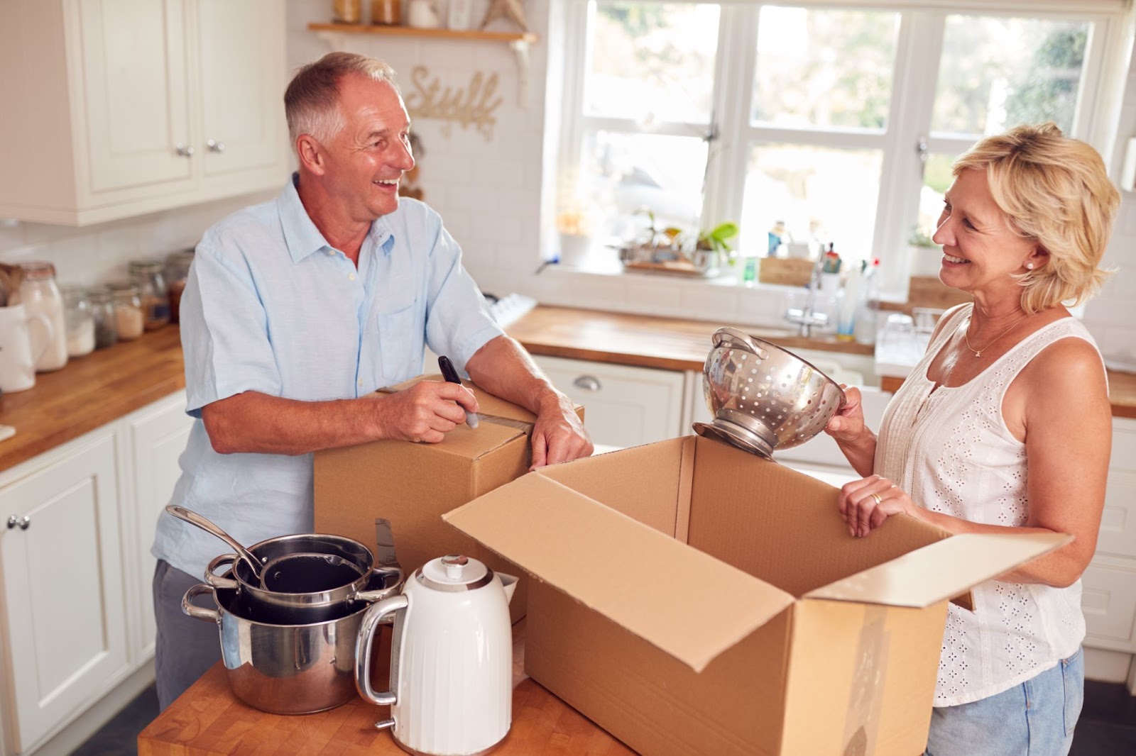 Two seniors laughing together as they downsize and pack up kitchen belongings for a move.