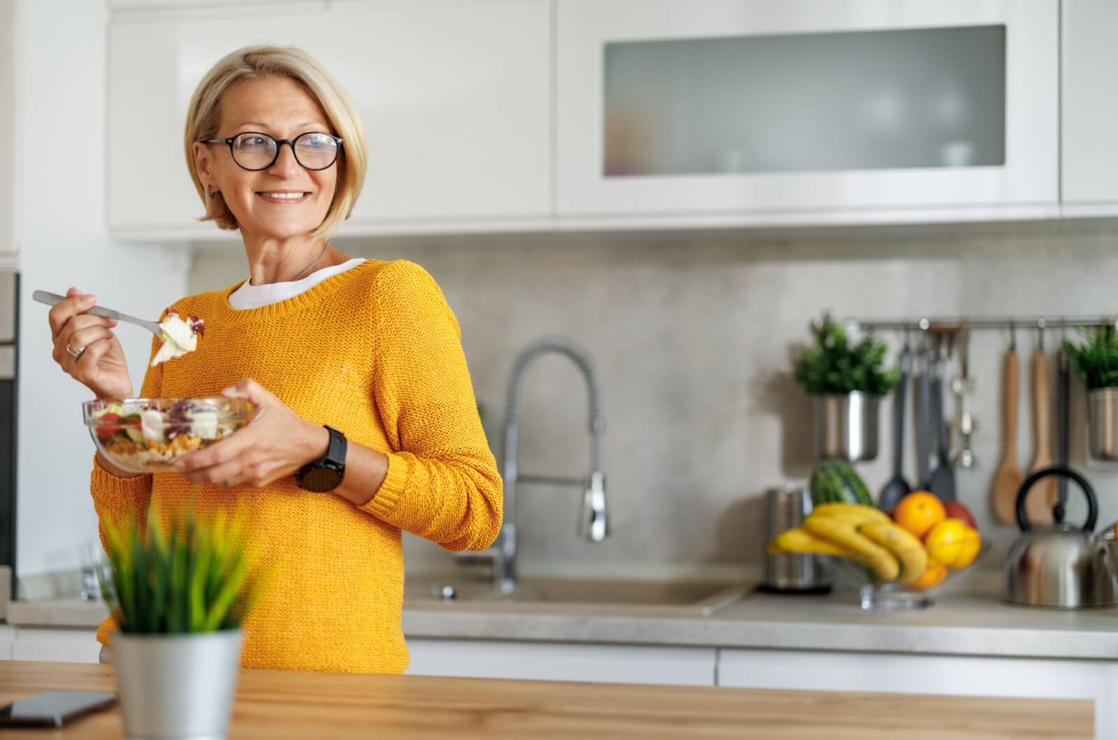 A smiling older adult enjoying a low-sodium meal in a kitchen.