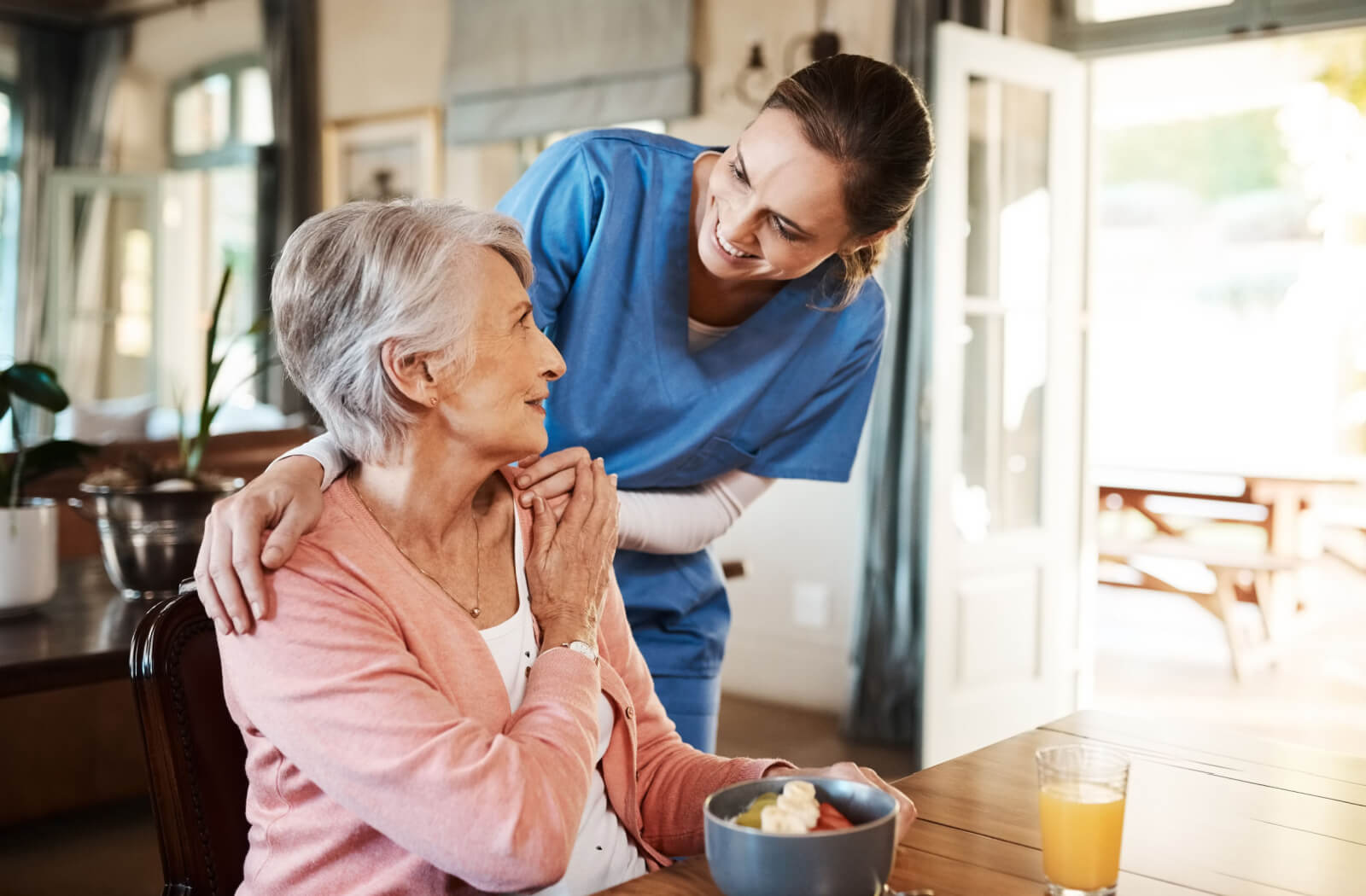 A caregiver checking on an older adult with dementia during breakfast while they smile at each other.