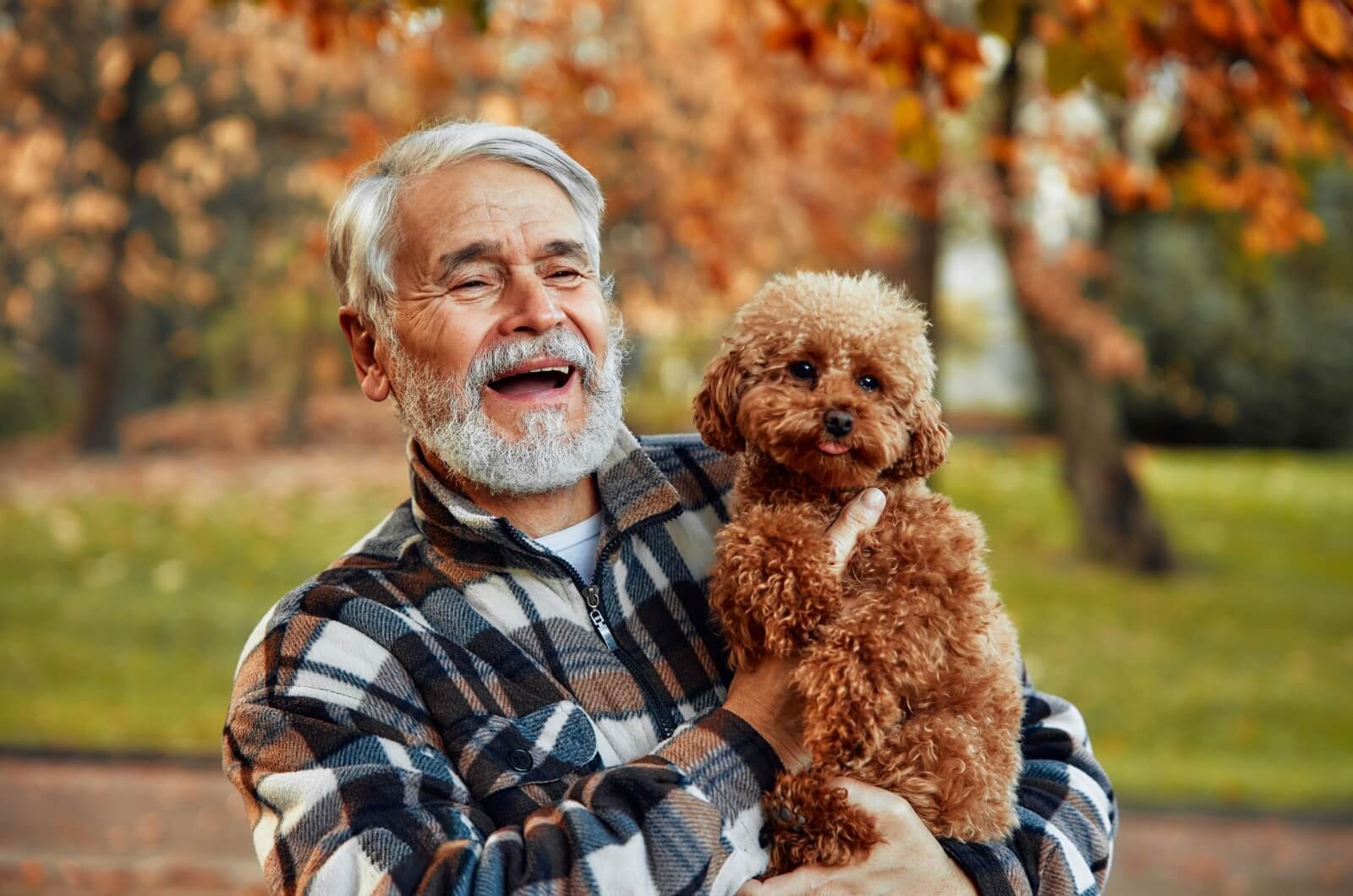 A happy older adult carrying a small dog in their arms while outdoors.