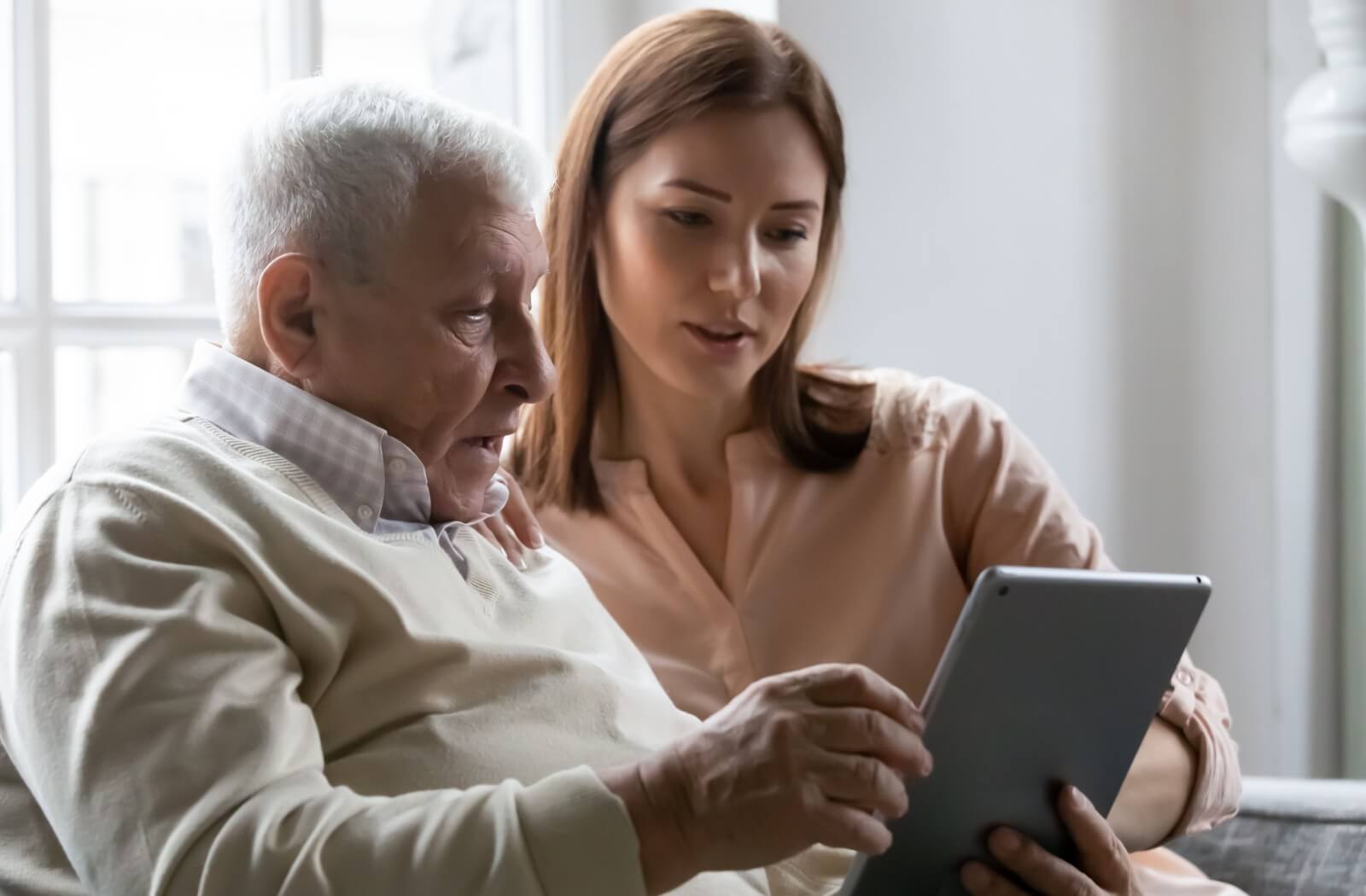 An adult child helps their senior parent with an app on their tablet to help organize their day.