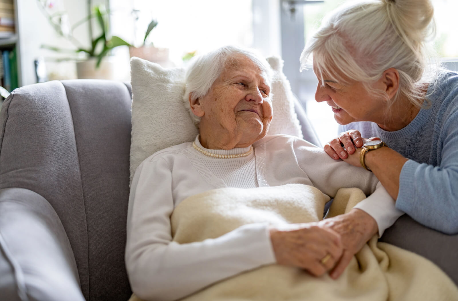 An adult smiling at their older parent with dementia as they lie down in memory care.
