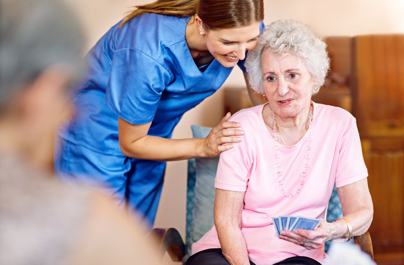 Care team member gently supporting older adult playing cards during a group activity in a warm welcoming care environment