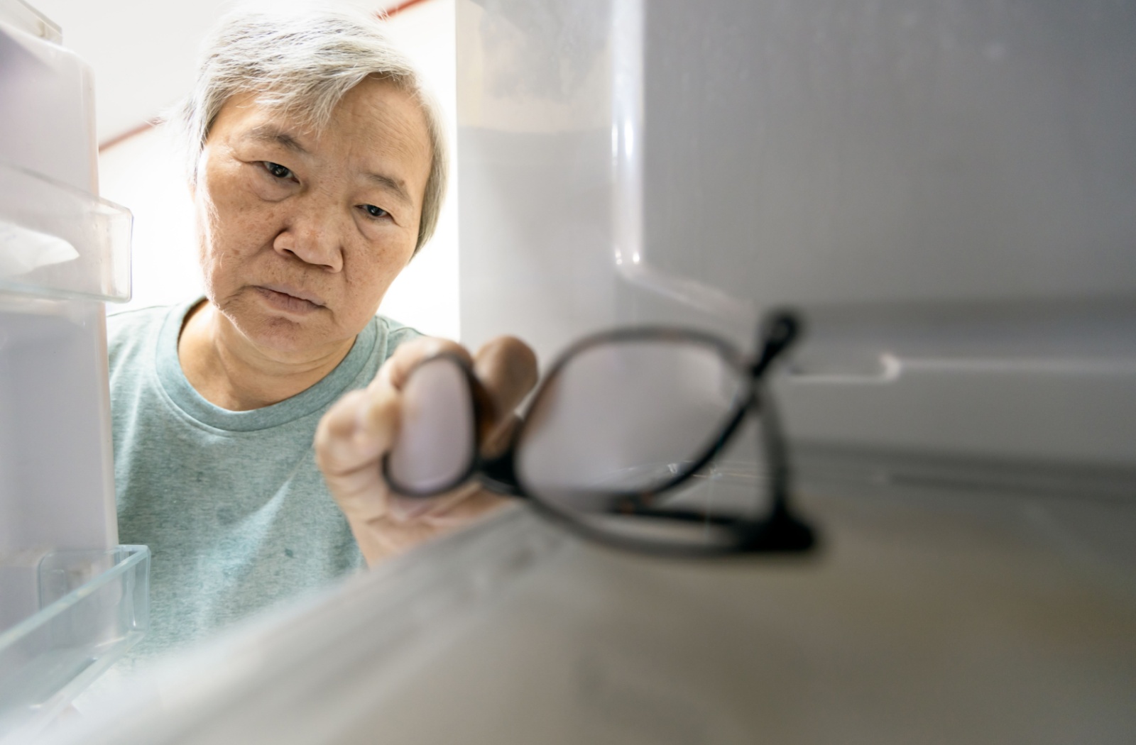 A senior with memory impairment symptoms forgets their glasses in the refrigerator, which could be a symptom of alzheimer's disease.