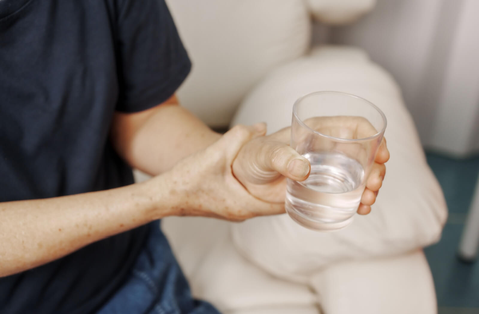 A close-up of the hands of a senior with Alzheimer's disease, struggling with holding a glass of water.

